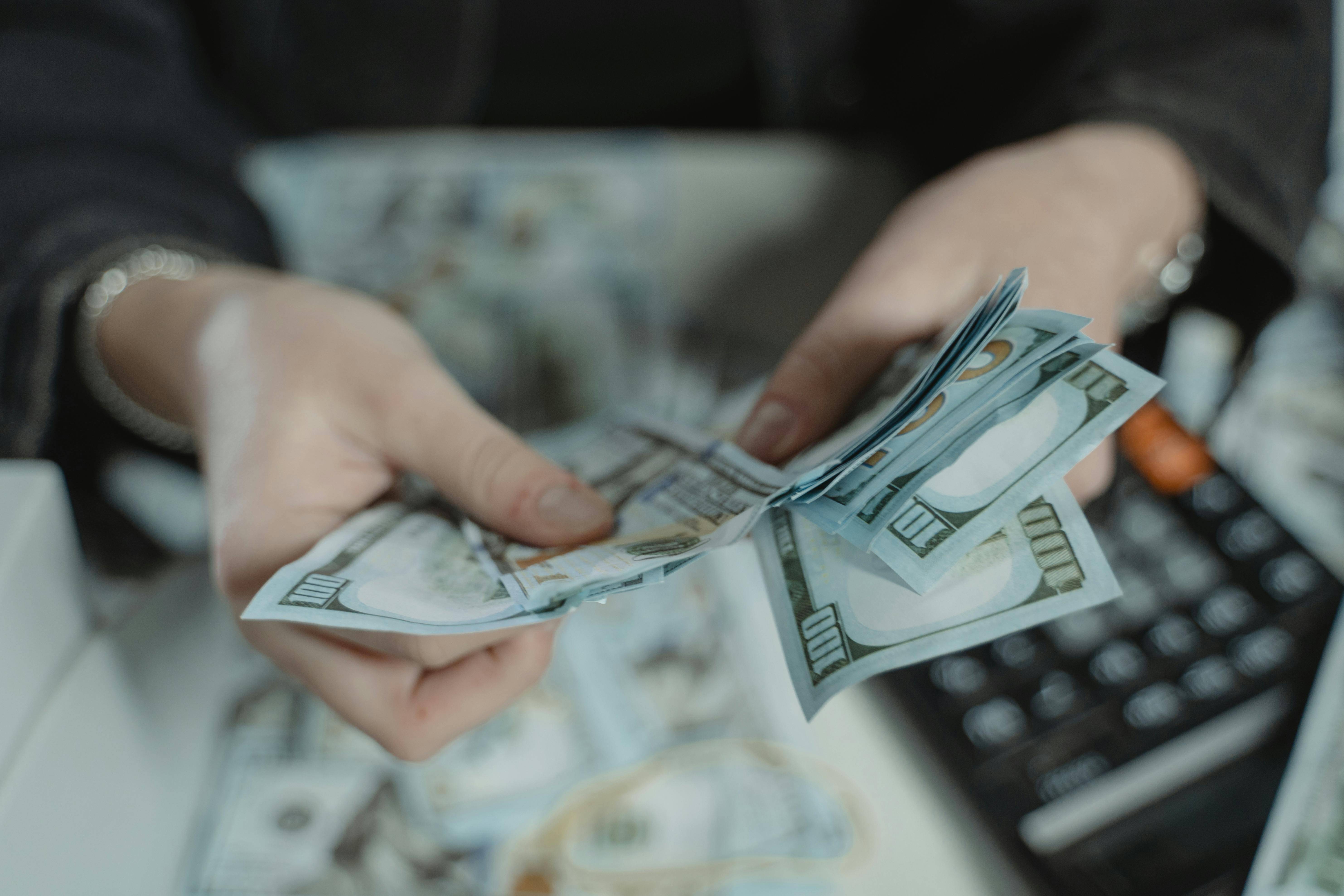 Person Counting Money with a calculator on a table in the background